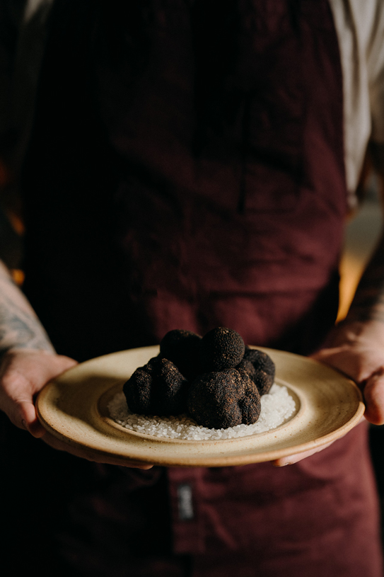Chef holding a plate of fresh black truffles over rock salt at Peonee Restaurant Canberra.