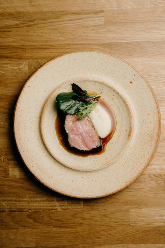 Meat dish served with creamy puree, jus, and greens on a ceramic plate at Peonee Restaurant Canberra.
