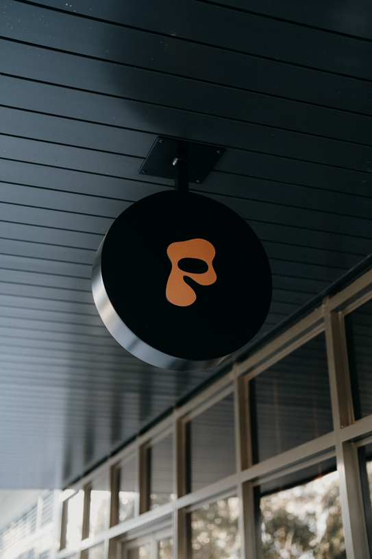 Peonee Restaurant black round sign with orange abstract logo hanging outside the restaurant in Canberra.