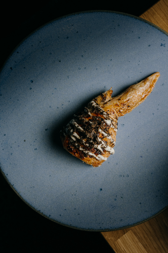 Crispy chicken wing drizzled with truffle sauce on a blue ceramic plate at Peonee Restaurant Canberra.